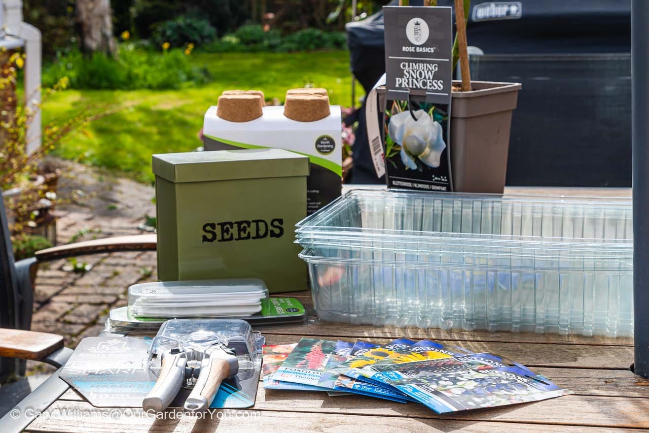 A selection of goodies from our first trip to a garden centre in 2022 featuring a new pair of secateurs, packets of seeds, labels, biodegradable pots and a white climbing rose.