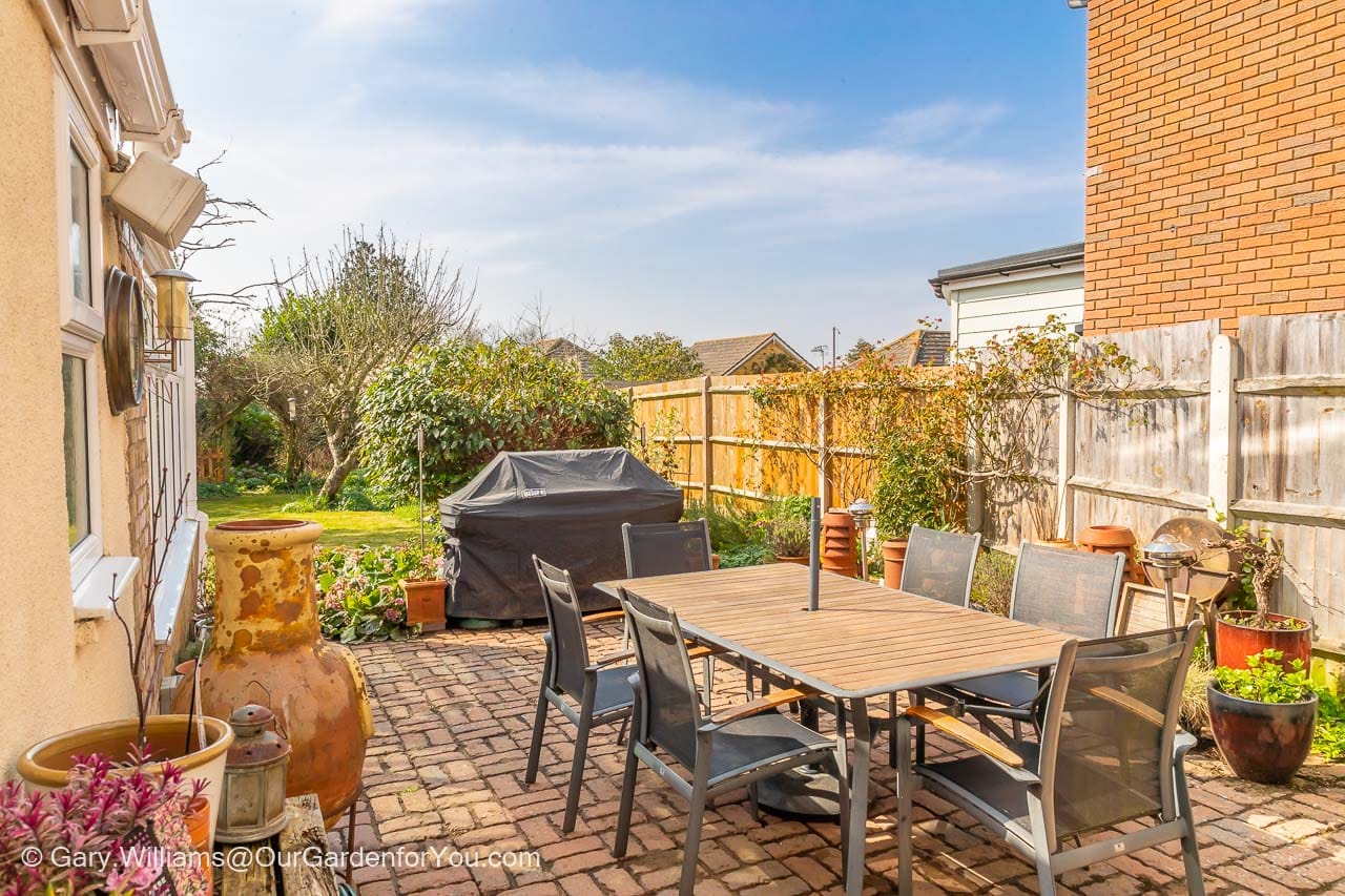 The patio laid out on a cross brick pattern with a 6 seater outdoor dining table and a large BBQ at the edge of the garden