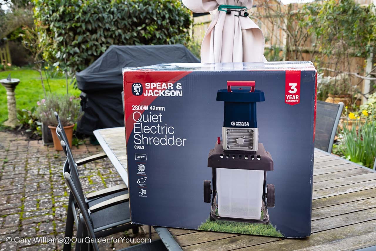A boxed Spear & Jackson quiet electric garden shredder sits on a patio table in a backyard garden. This practical tool is ideal for tackling winter pruning waste during February garden jobs.